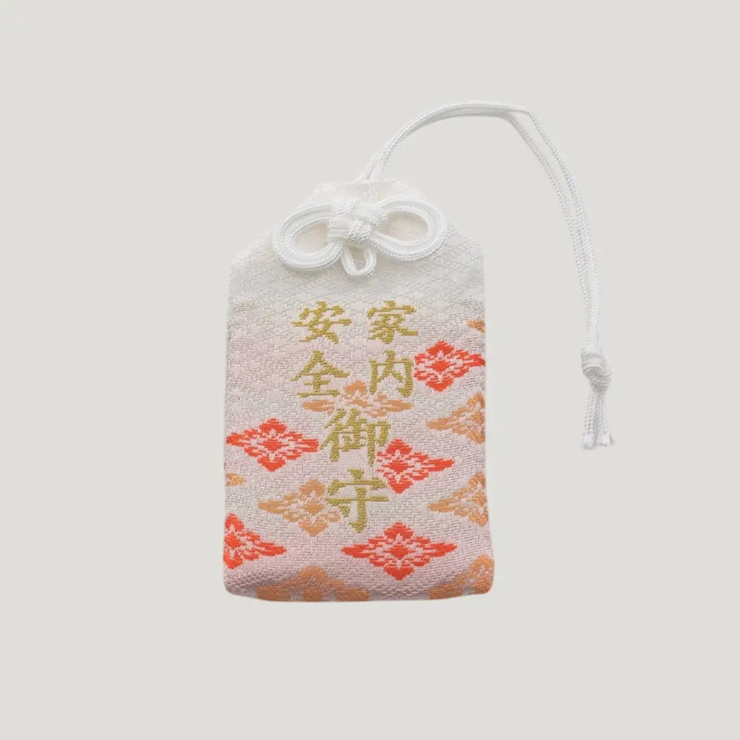 Front view of a traditional Japanese omamori for family safety from Saijo Inari temple, with white and orange/gold fabric and the kanji for 'family safety'.