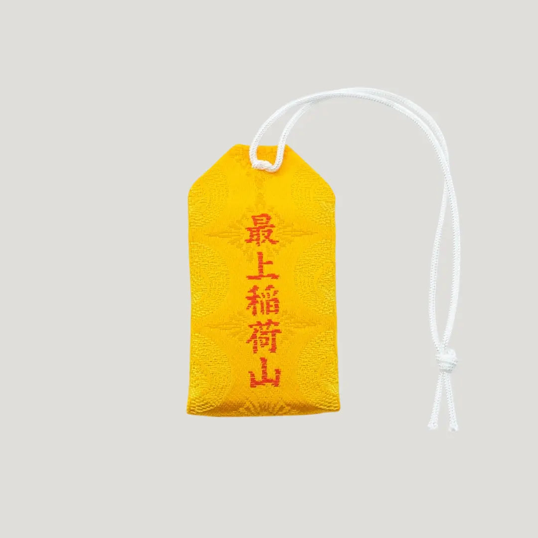 Back view of a traditional Japanese omamori for money luck from Saijo Inari temple, showing subtle gold patterns on a vibrant yellow fabric.