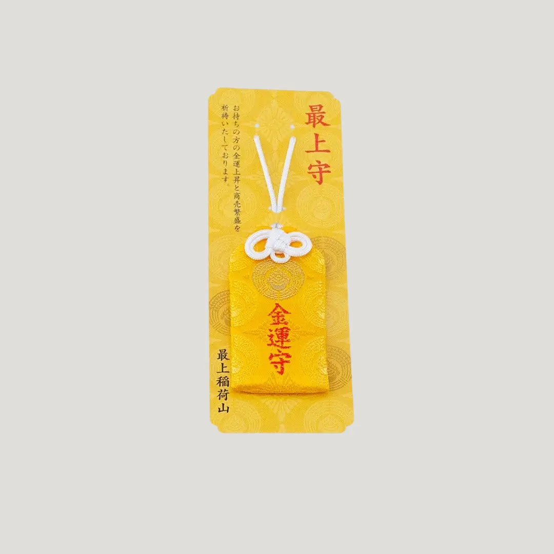 A traditional Japanese omamori for money luck from Saijo Inari temple, showing a yellow fabric with gold embroidered kanji, displayed on its original card.