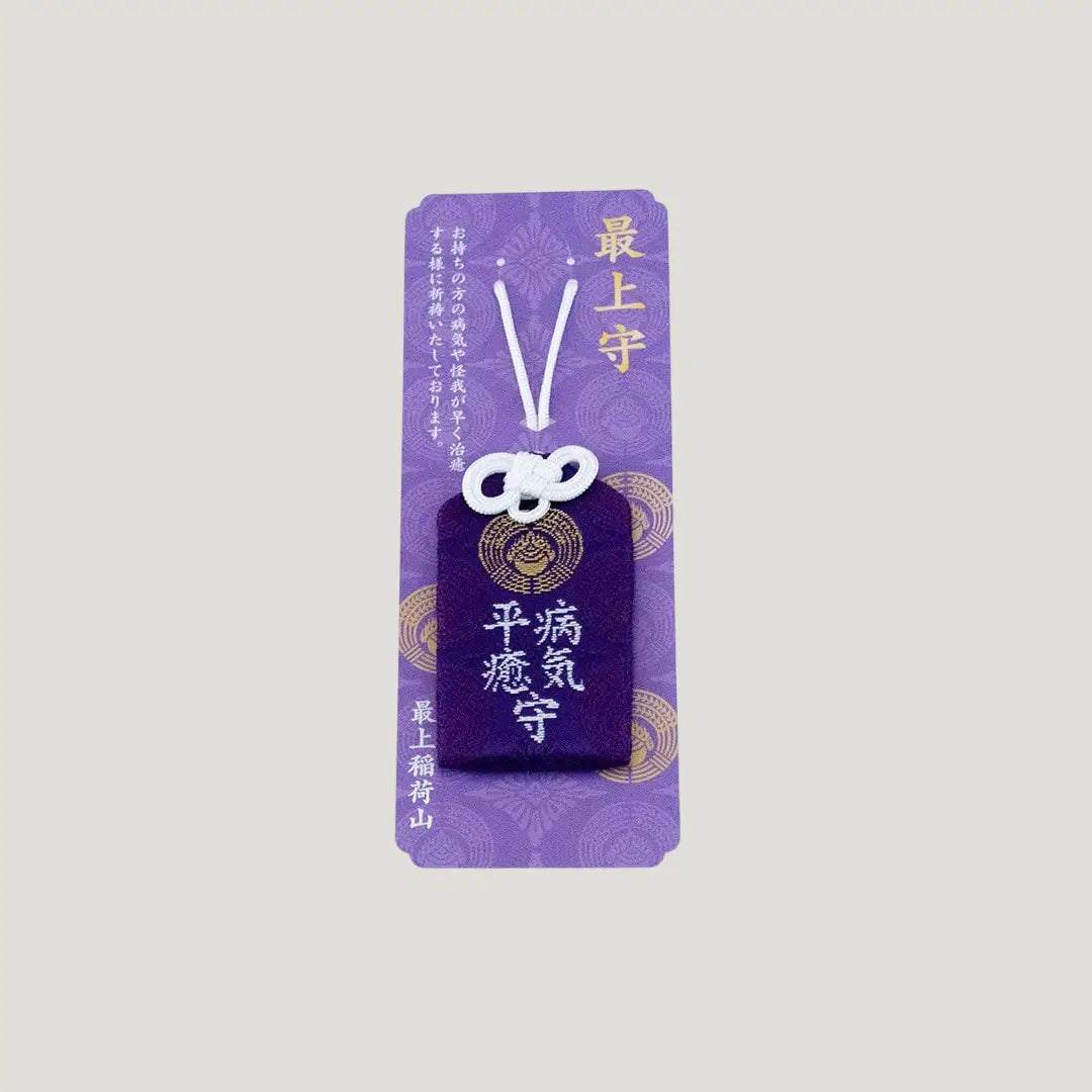 A traditional Japanese omamori for sickness recovery from Saijo Inari temple, showing a deep purple fabric with gold embroidered kanji on its original card.
