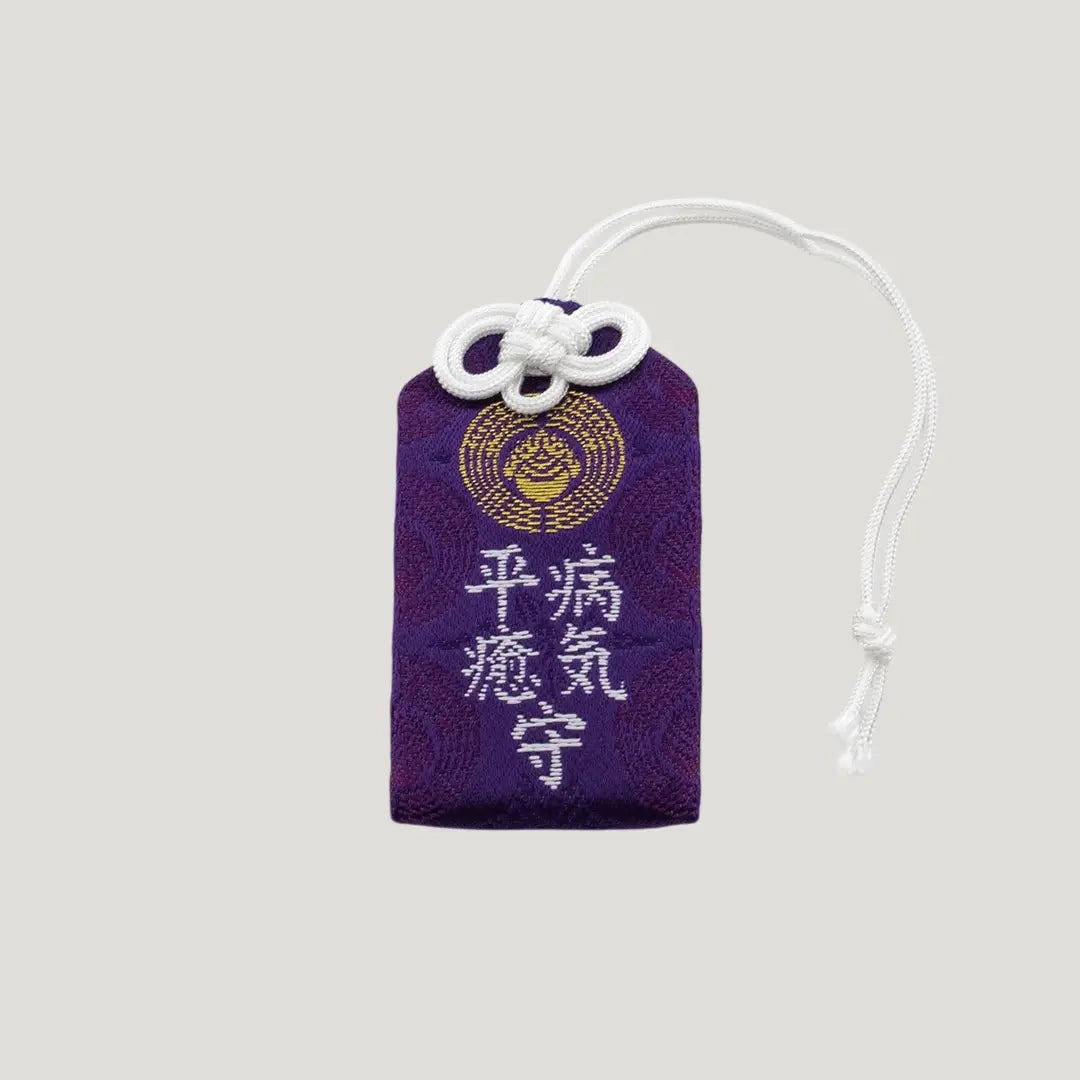 Front view of a traditional Japanese omamori for sickness recovery from Saijo Inari temple, showing deep purple fabric with gold embroidery.