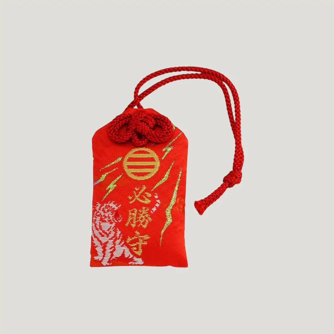 Front of Sure Victory Omamori from Shirasaki Shrine – red charm with embroidered white tiger, gold symbol, and red cord