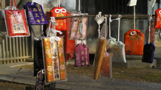 Various types of Japanese Omamori hanging on display at a traditional shrine, showing charms for protection, health, love, and safe travel