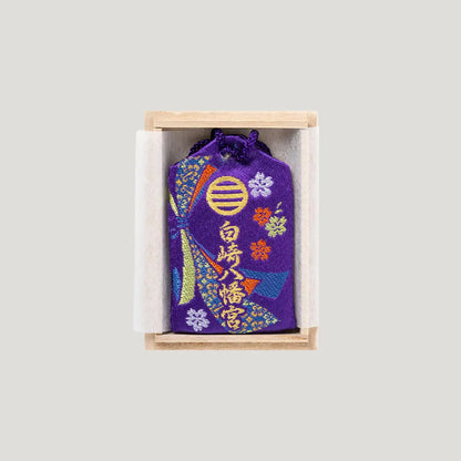 Back of Career Success Omamori with purple embroidery in wooden box showing Shirasaki Shrine name