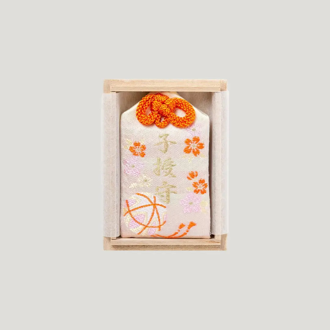 Child Blessing Omamori from Shirasaki Hachimangu Shrine, cream embroidered charm with orange cord in a wooden box for family blessings and new beginnings.