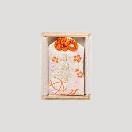 Child Blessing Omamori from Shirasaki Hachimangu Shrine, cream embroidered charm with orange cord in a wooden box for family blessings and new beginnings.
