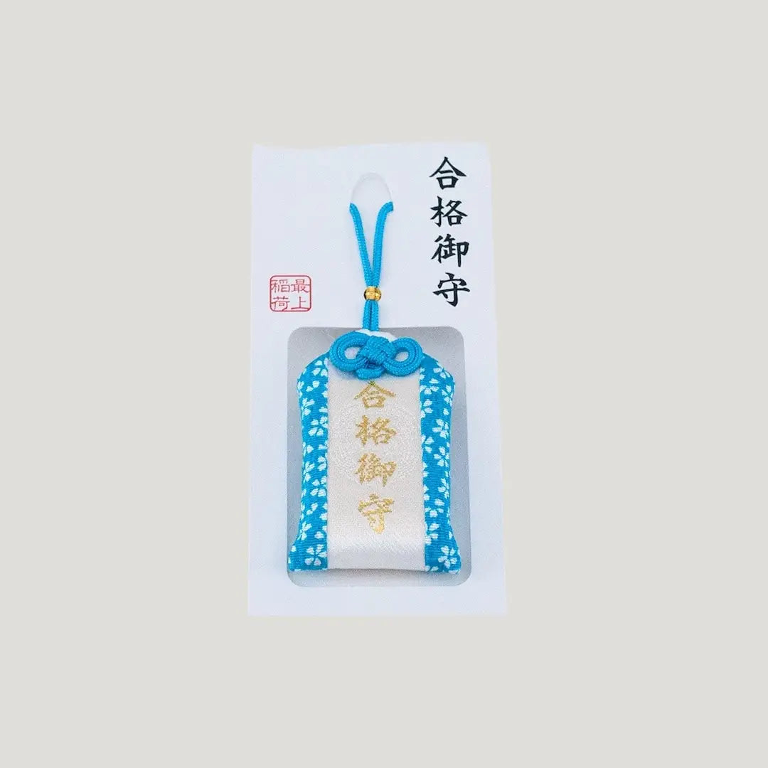 A traditional Japanese omamori for exam success from Saijo Inari temple, with blue and white fabric and the kanji for 'success', shown on its original white and blue backing card.