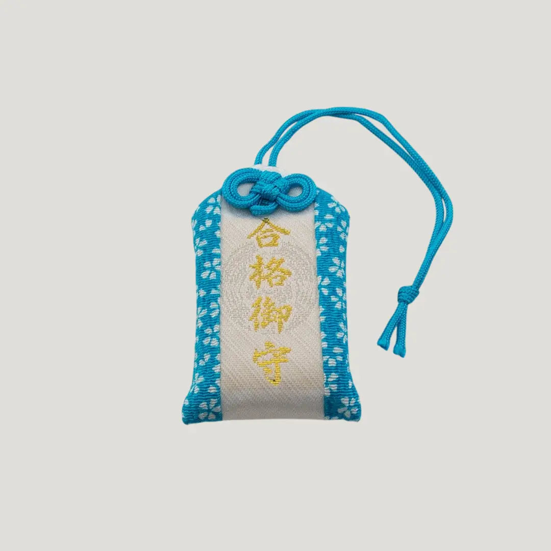 Front view of a traditional Japanese omamori for exam success from Saijo Inari temple, with blue and white fabric and the kanji for 'success'.