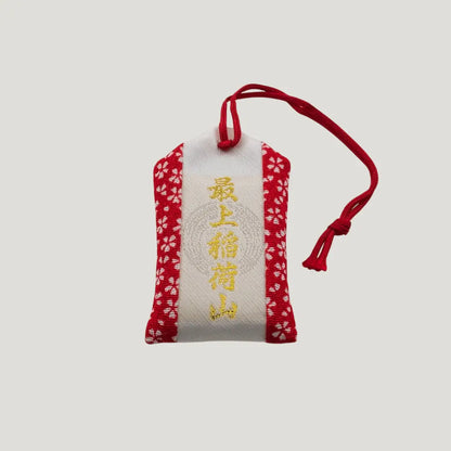 Back view of a traditional Japanese omamori for exam success from Saijo Inari temple, with red and white fabric and a simple design.