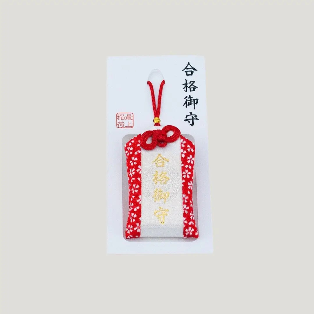 A traditional Japanese omamori for exam success from Saijo Inari temple, with red and white fabric and the kanji for 'success', shown on its original white and red backing card.