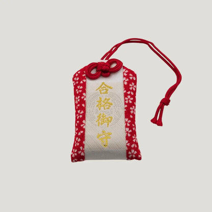Front view of a traditional Japanese omamori for exam success from Saijo Inari temple, with red and white fabric and the kanji for 'success'.