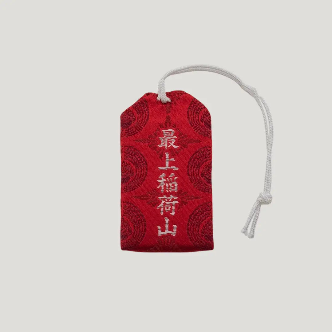 Back view of a traditional Japanese omamori for good fortune from Saijo Inari temple, with red and gold fabric and a repeating pattern.
