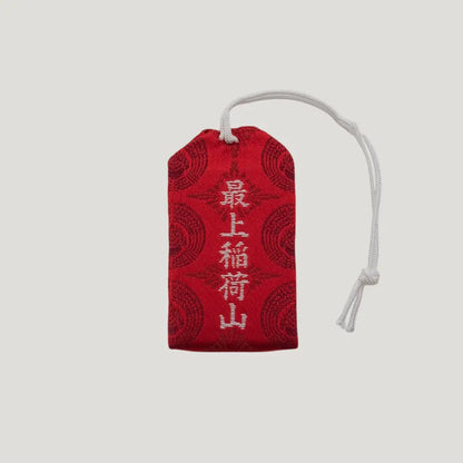 Back view of a traditional Japanese omamori for good fortune from Saijo Inari temple, with red and gold fabric and a repeating pattern.