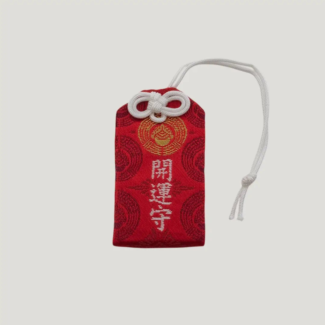 Front view of a traditional Japanese omamori for good fortune from Saijo Inari temple, with red and gold fabric and the kanji for 'good fortune'.