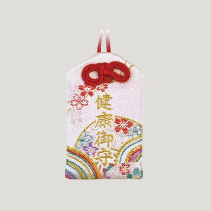Front view of a traditional Japanese health omamori from Saijo Inari temple, showing white fabric with colorful fan and floral embroidery and red cord.