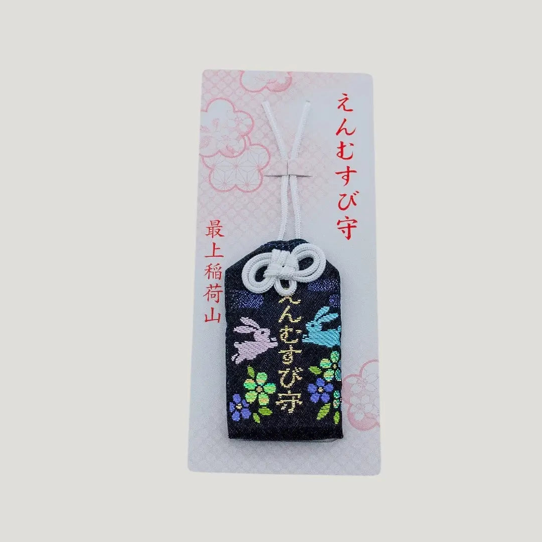 A traditional Japanese omamori for love and relationships from Saijo Inari temple, showing a black fabric with rabbit and floral embroidery on its original card.