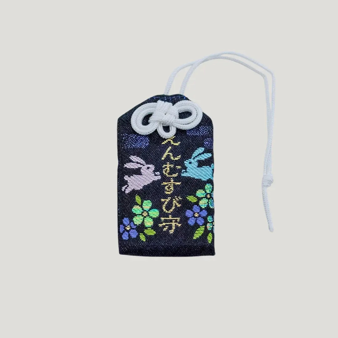 Front view of a traditional Japanese omamori for love and relationships from Saijo Inari temple, with black fabric and embroidered rabbits and flowers.