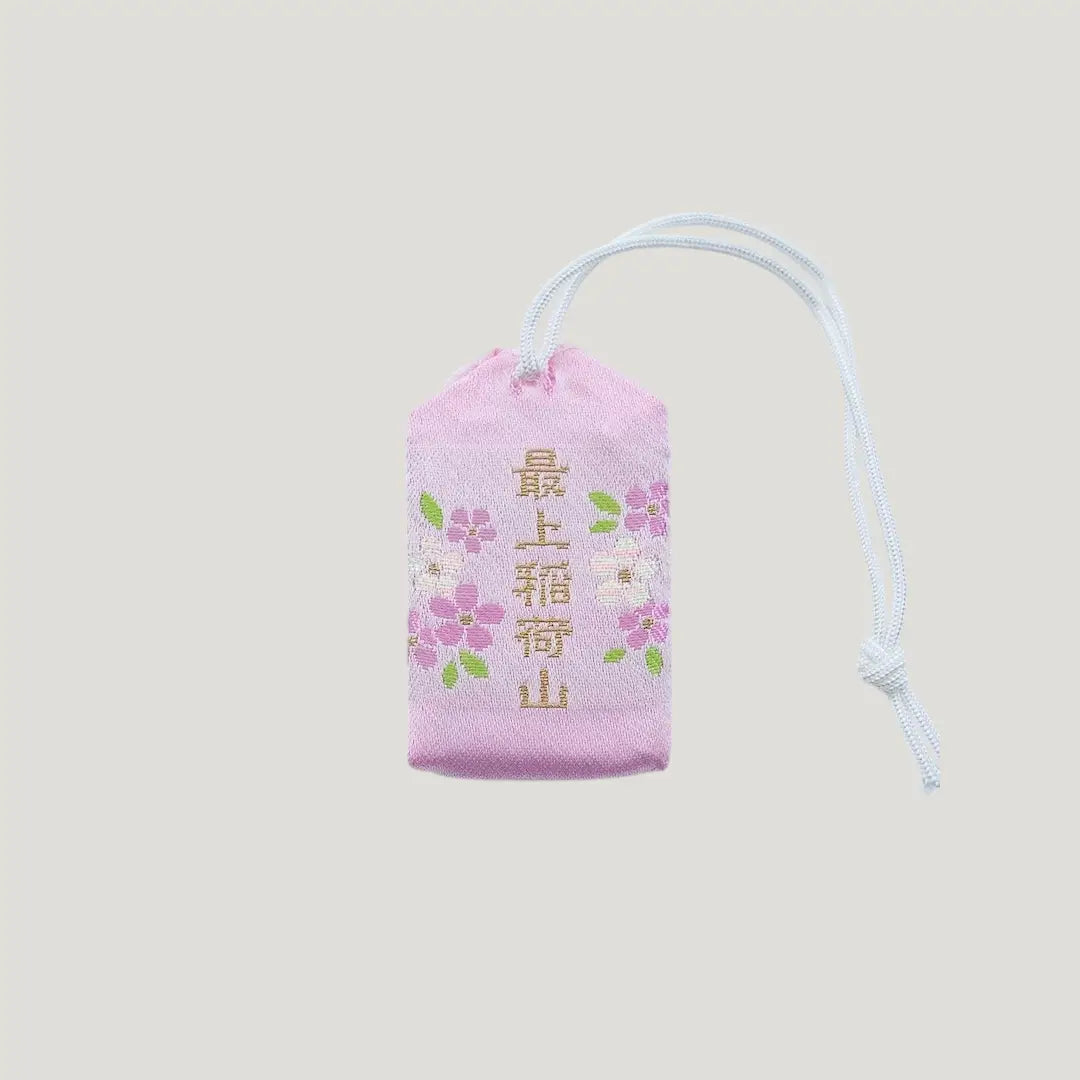 Back view of a traditional Japanese omamori for love and relationships from Saijo Inari temple, with a light peach fabric and a subtle design.