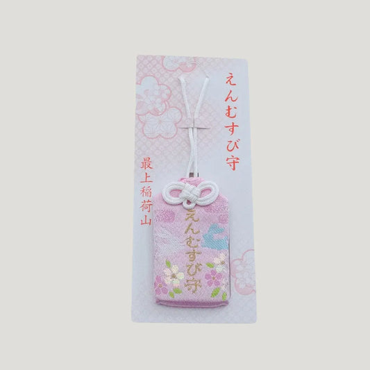 A traditional Japanese omamori for love and relationships from Saijo Inari temple, showing a light peach fabric with floral embroidery on its original card.