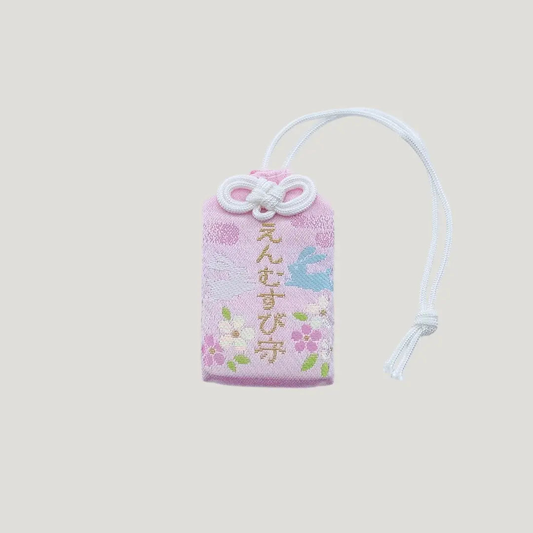Front view of a traditional Japanese omamori for love and relationships from Saijo Inari temple, with a light peach fabric and embroidered rabbits and flowers.