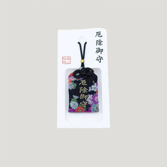 A traditional Japanese omamori for misfortune protection from Saijo Inari temple, with a black fabric and a floral pattern, shown on its original card.