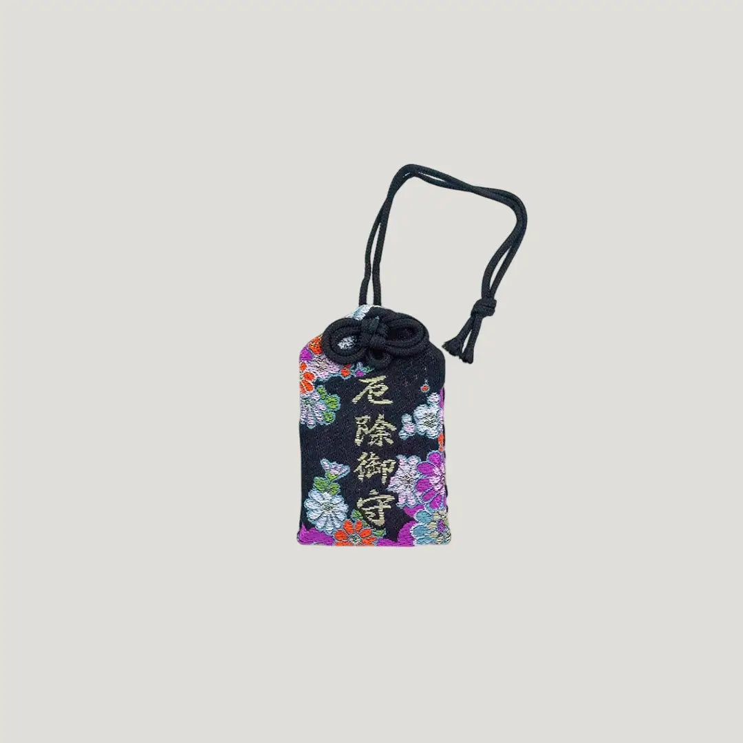 Front view of a traditional Japanese omamori for misfortune protection from Saijo Inari temple, with a black fabric and a floral pattern.