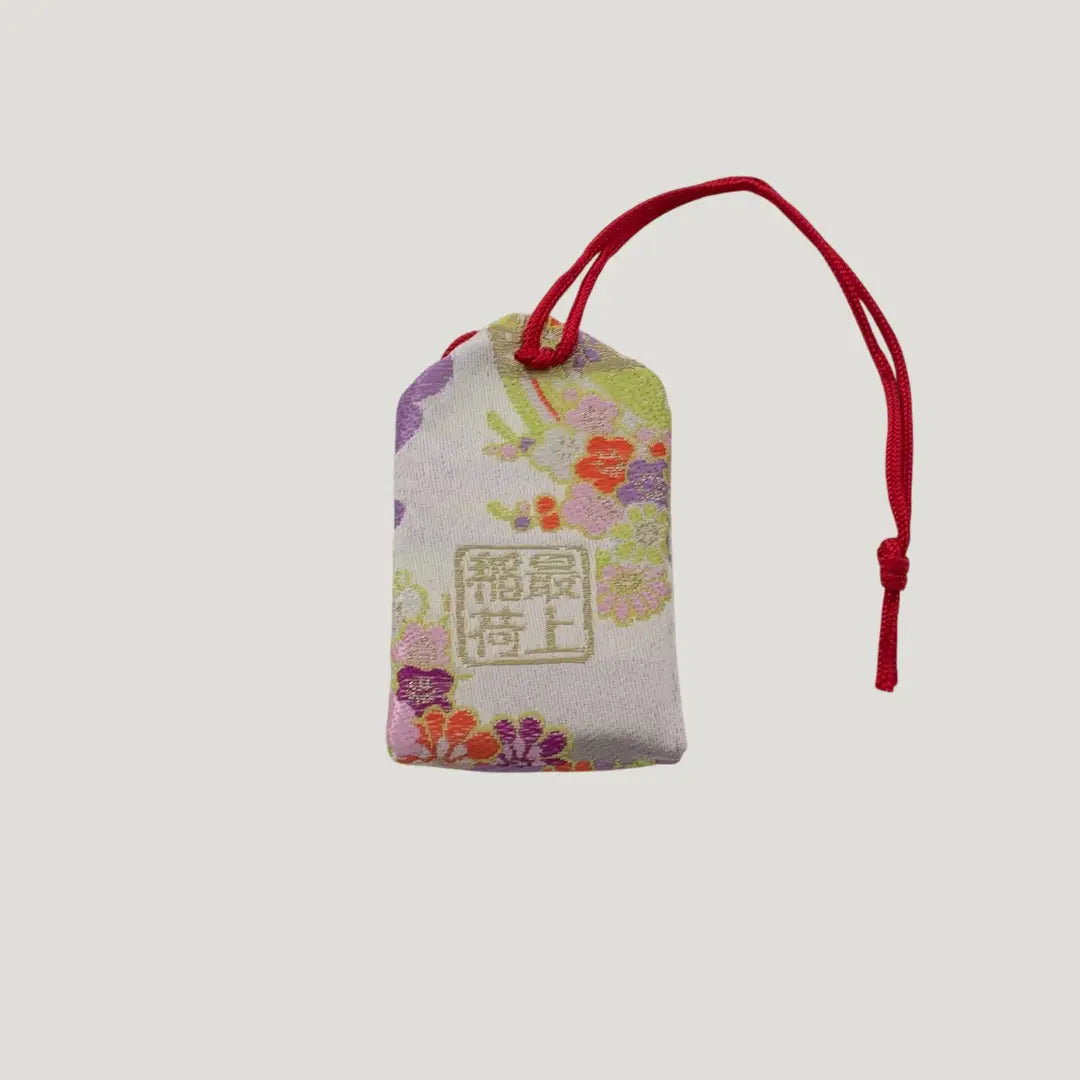 Back view of a traditional Japanese omamori for misfortune protection from Saijo Inari temple, with a white fabric and a subtle design.