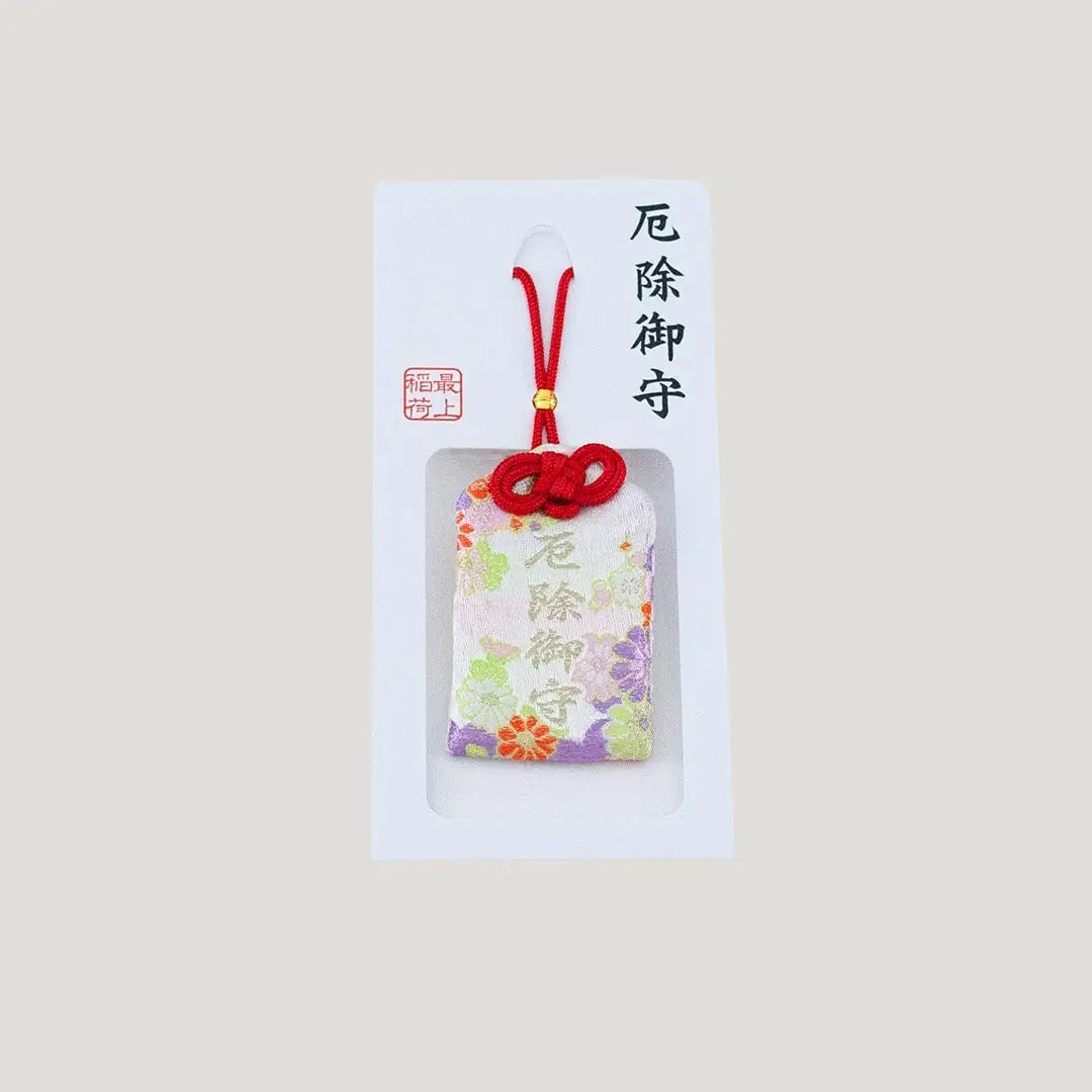 A traditional Japanese omamori for misfortune protection from Saijo Inari temple, with a white fabric and a floral pattern, shown on its original card.