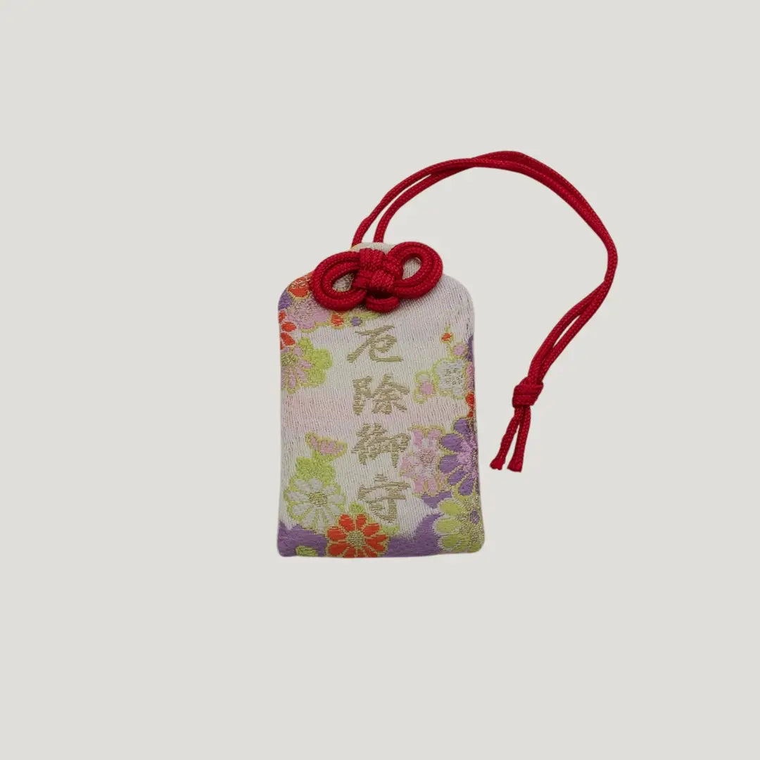 Front view of a traditional Japanese omamori for misfortune protection from Saijo Inari temple, with a white fabric and a floral pattern.
