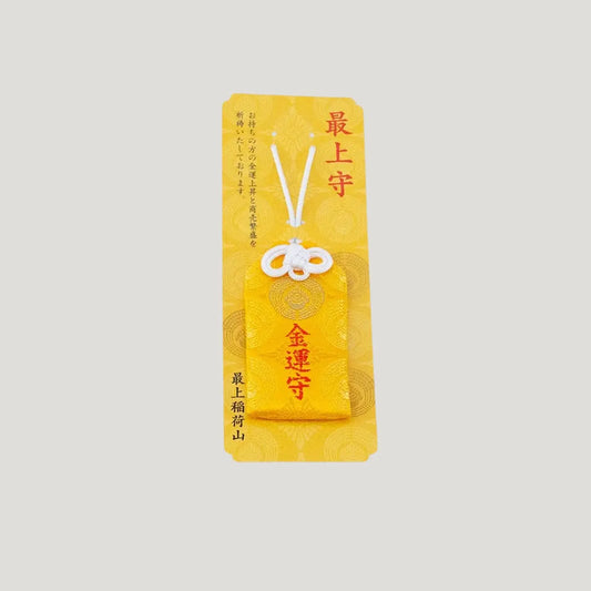 A traditional Japanese omamori for money luck from Saijo Inari temple, showing a yellow fabric with gold embroidered kanji, displayed on its original card.