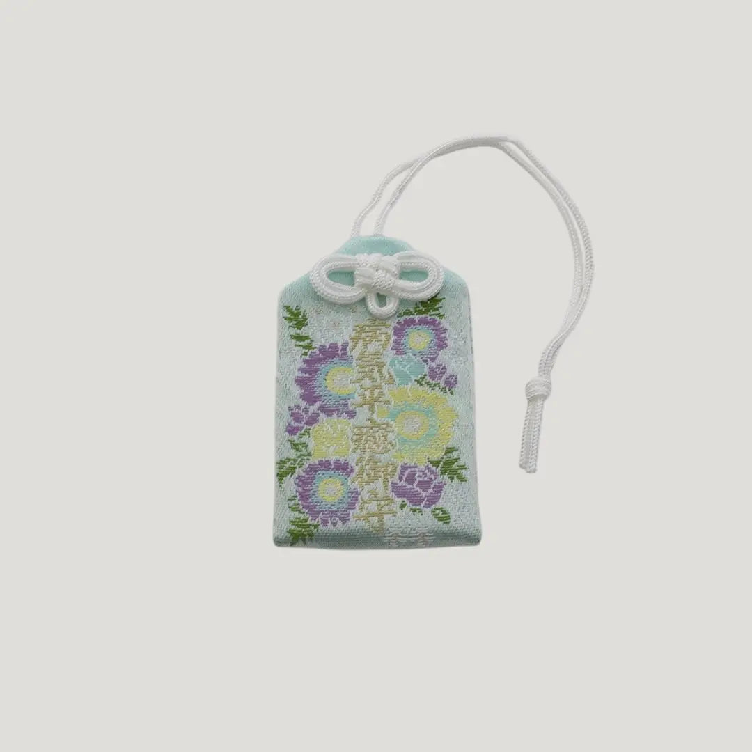 Front view of a traditional Japanese omamori for sickness recovery from Saijo Inari temple, with a light blue fabric and delicate floral embroidery.