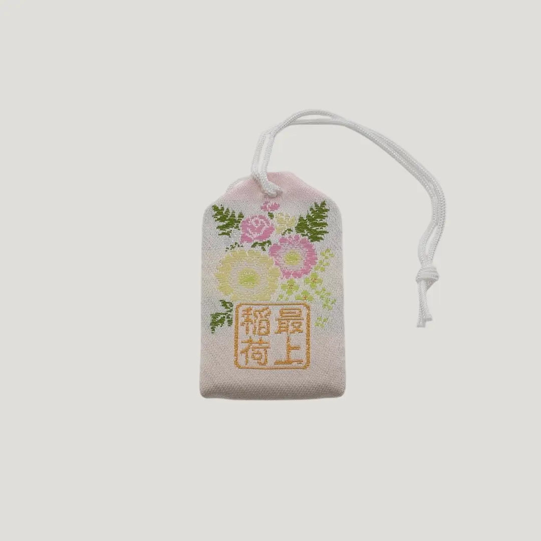 Back view of a traditional Japanese omamori for sickness recovery from Saijo Inari temple, with a white fabric and delicate floral embroidery.