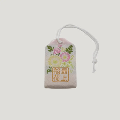 Back view of a traditional Japanese omamori for sickness recovery from Saijo Inari temple, with a white fabric and delicate floral embroidery.