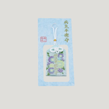 A traditional Japanese omamori for sickness recovery from Saijo Inari temple, showing a light blue fabric with delicate floral embroidery on its original card.