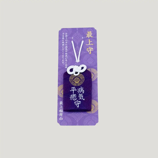 A traditional Japanese omamori for sickness recovery from Saijo Inari temple, showing a deep purple fabric with gold embroidered kanji on its original card.
