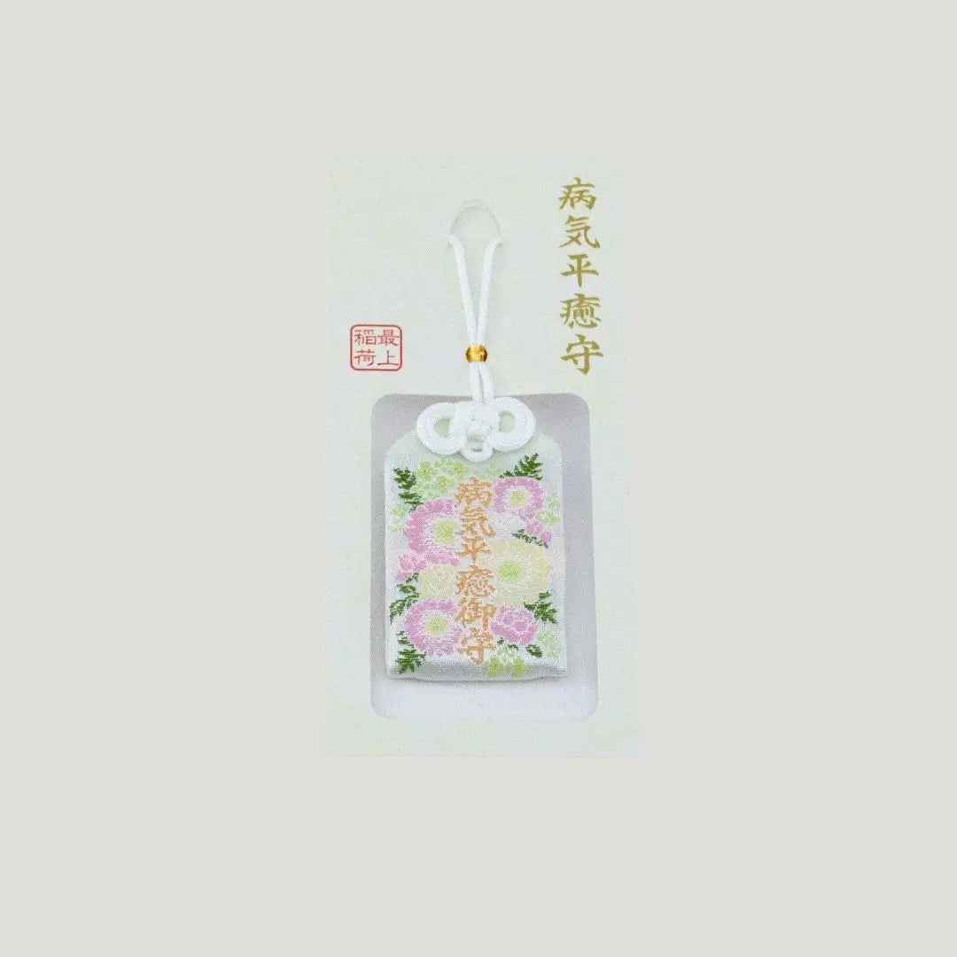 A traditional Japanese omamori for sickness recovery from Saijo Inari temple, showing a white fabric with delicate floral embroidery on its original card.