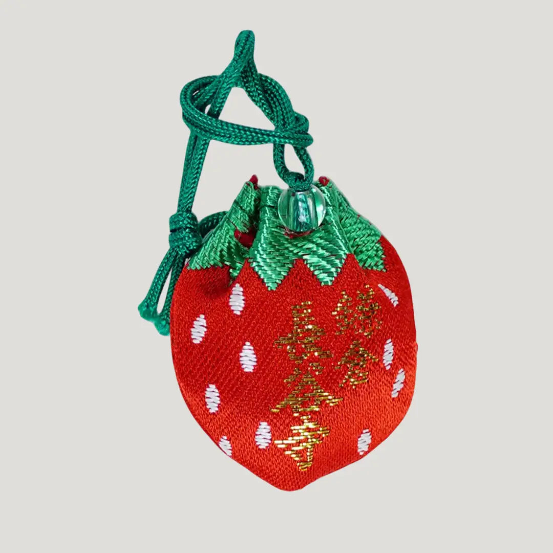 Back side of strawberry-shaped 願い叶う守 (Wish-Fulfillment Omamori) from Hasedera Temple – red charm with green cord, gold embroidered Hasedera temple name, and white seed design
