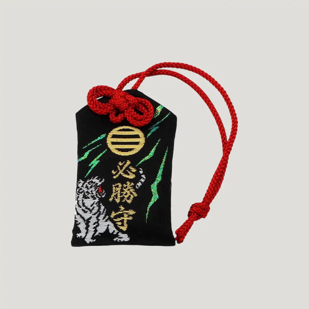 Front of Sure Victory Omamori from Shirasaki Shrine – black charm with embroidered white tiger, gold symbol, and red cord
