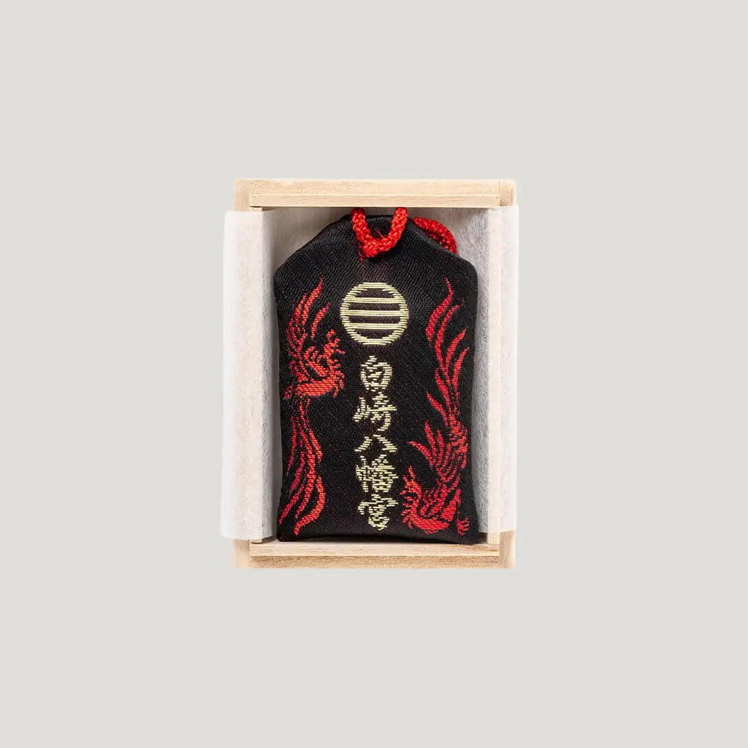 Wish Fulfillment Omamori (心願成就お守り) back side – black charm with golden Shirasaki Shrine crest and red phoenix motif, presented in a wooden box