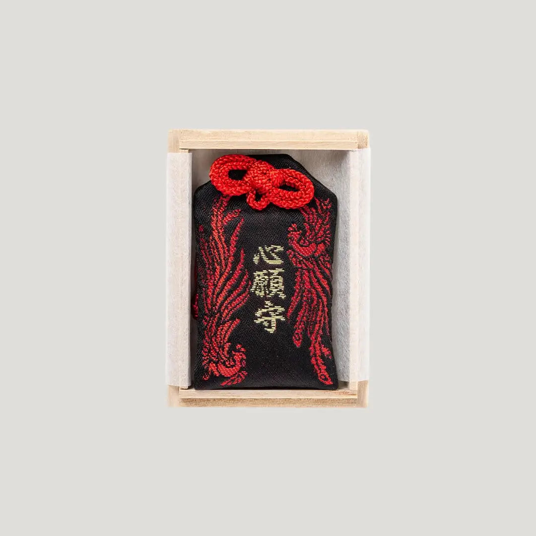 Wish Fulfillment Omamori (心願成就お守り) – black Japanese charm with red phoenix-style bugaku design and red cord, presented in a wooden box from Shirasaki Shrine